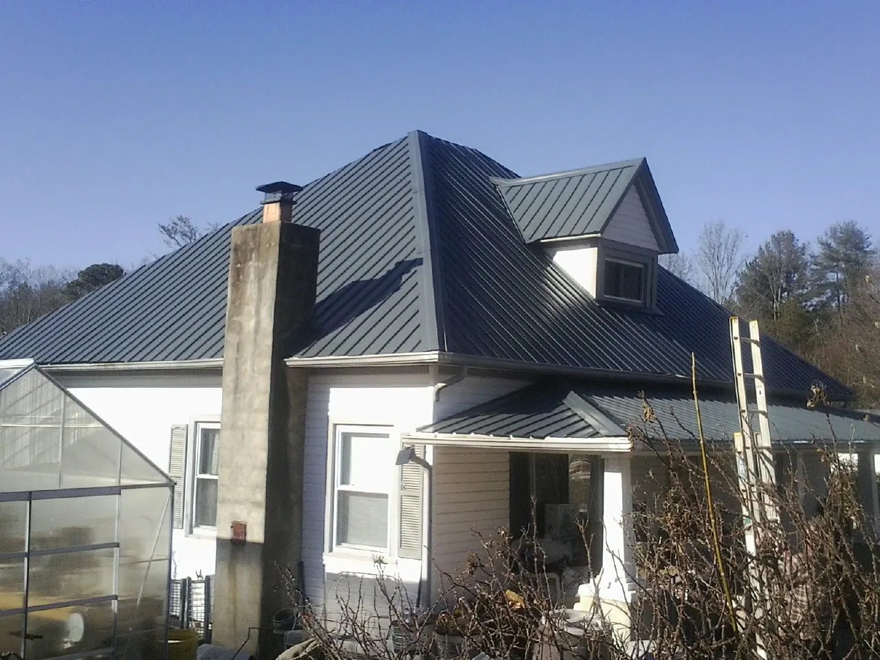 Dark blue standing seam metal roof on a white farmhouse with dormer — Slate & Tile Roof Repair by Roofing Brothers in Homer City