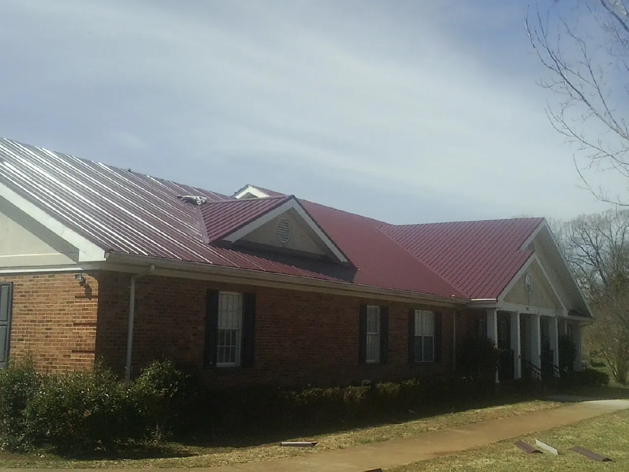 Red metal roof with gabled entries on a long brick building, from a Hail Damage Roof Repair job in Homer City