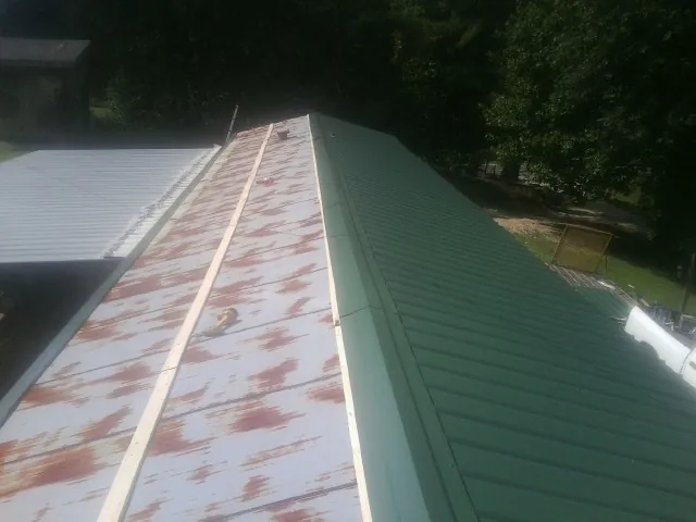 Old rusted panels beside newly installed green metal roofing — Wind Damage Roof Repair by Roofing Brothers in Homer City