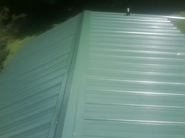 New green metal panels meeting at the ridge of a roof — Flat Roof Repair work by our crew in Homer City