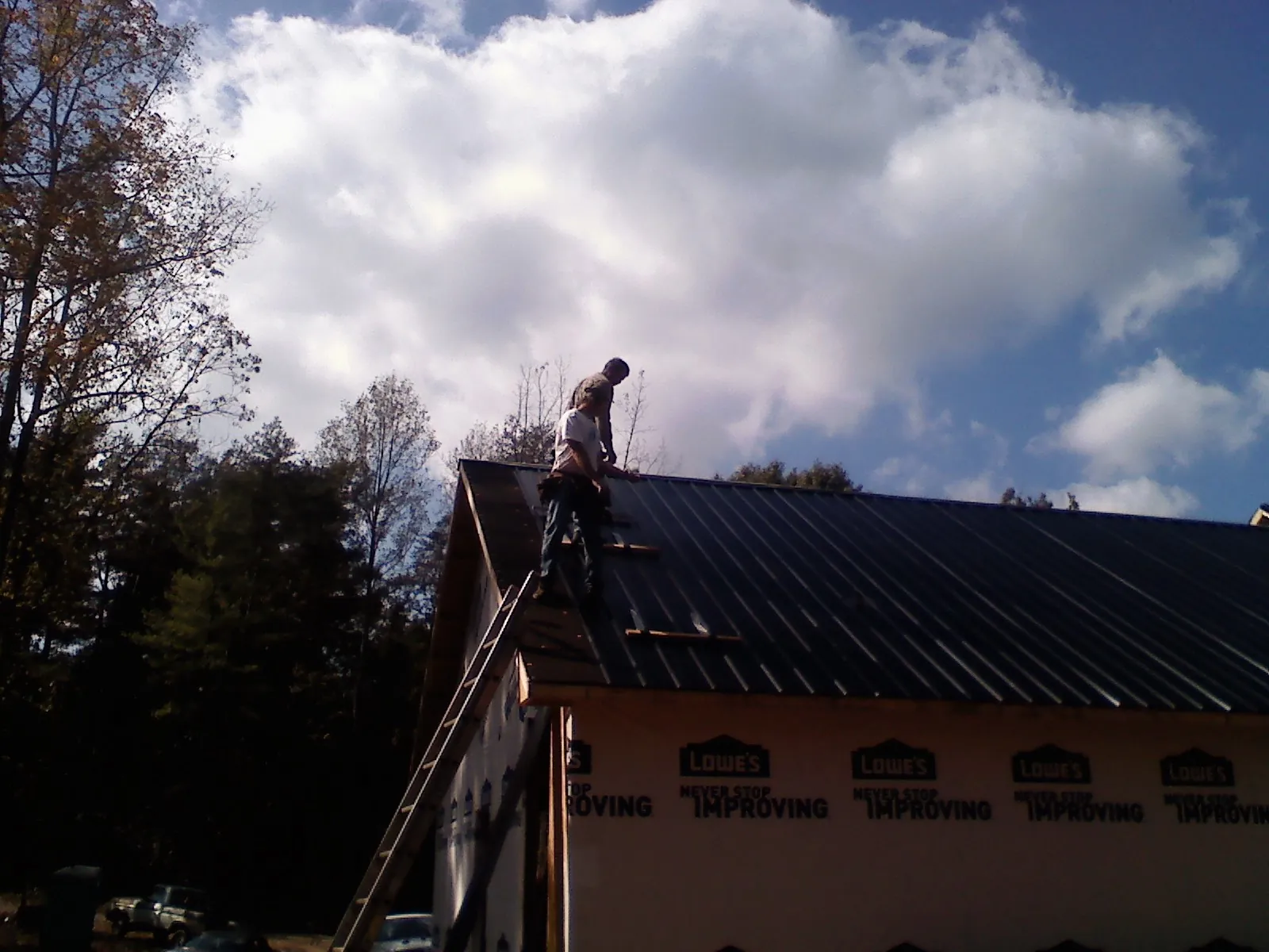 Roofer fastening dark metal panels high against a cloudy sky, from a Roof Inspection job in Homer City