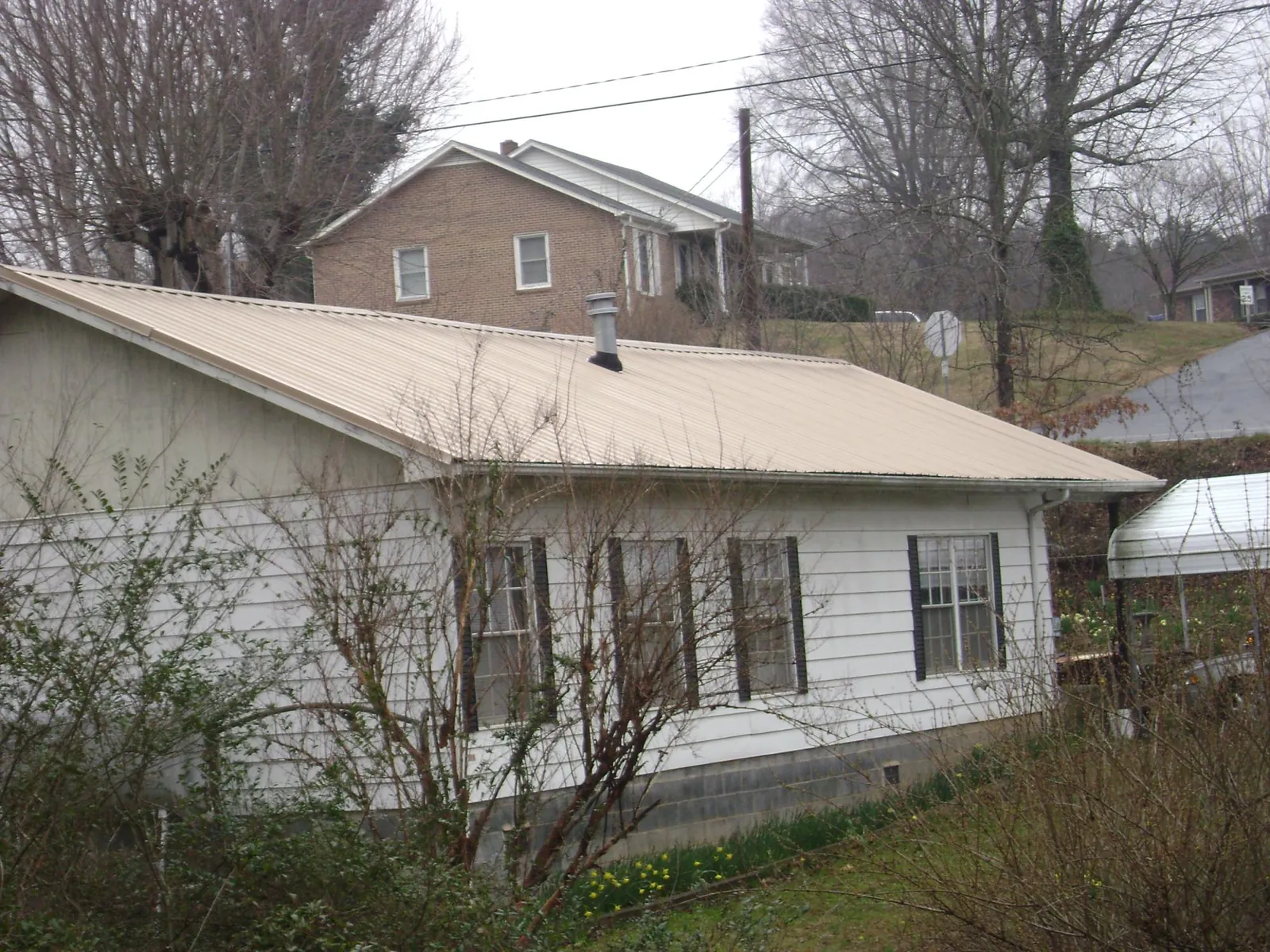 Tan metal roof on a white sided house set into a hillside — Commercial Roofing by Roofing Brothers in Homer City