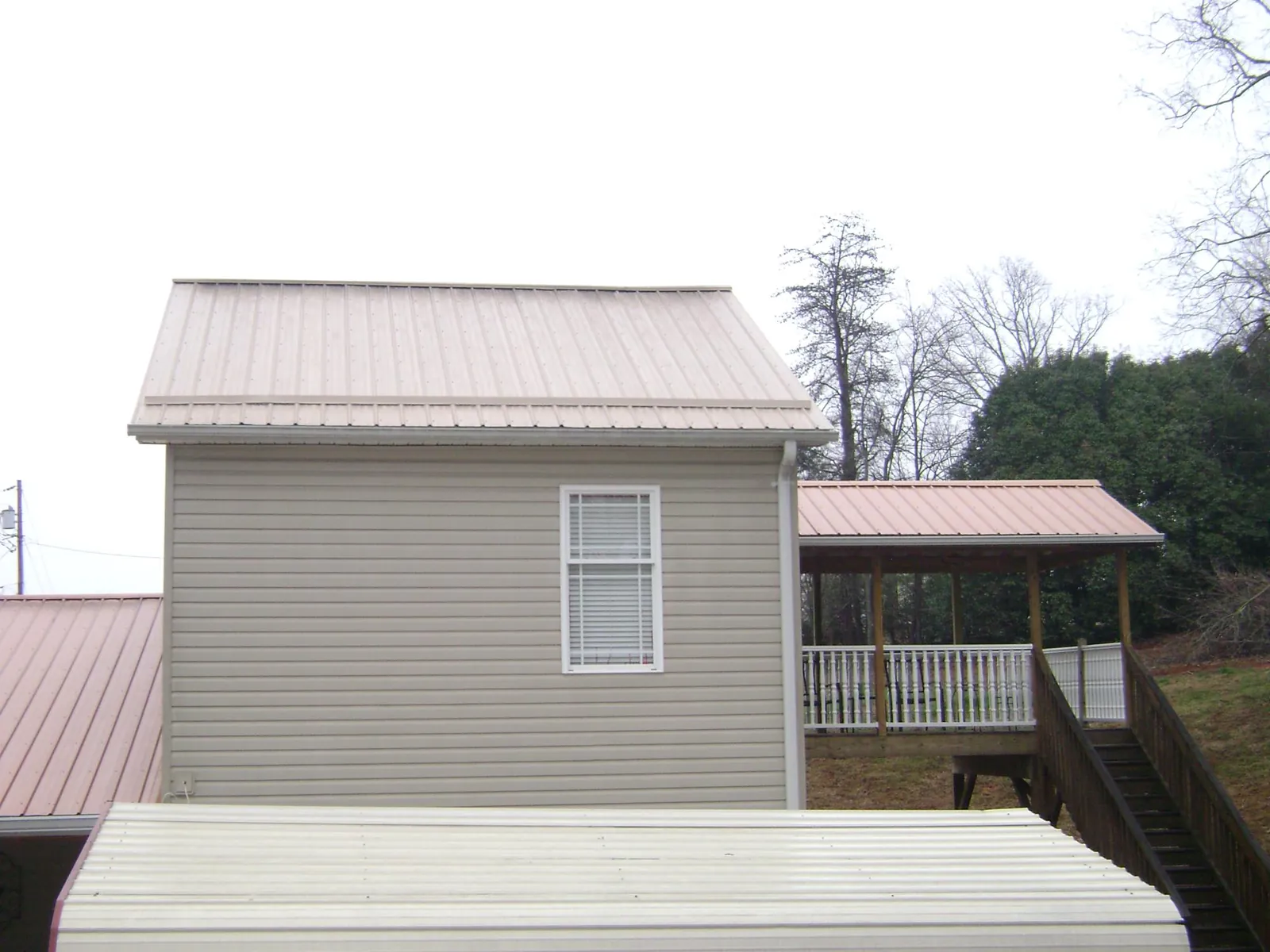 Tan metal roofs on a two story addition and attached porch, from a Roof Replacement job in Homer City